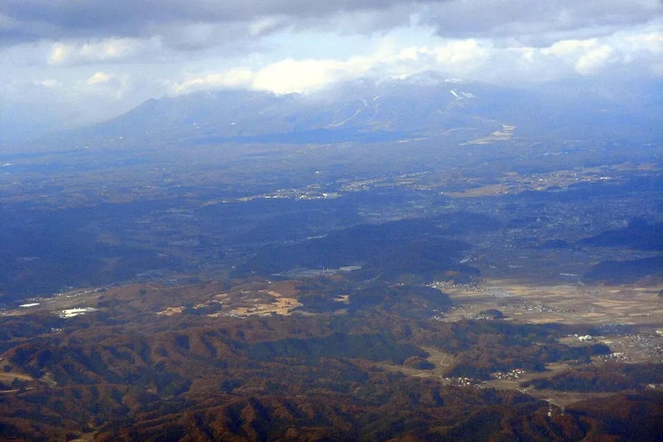 雲のかかる那須連山の手前に、林と畑が広がるなだらかな高原を見下ろす遠景